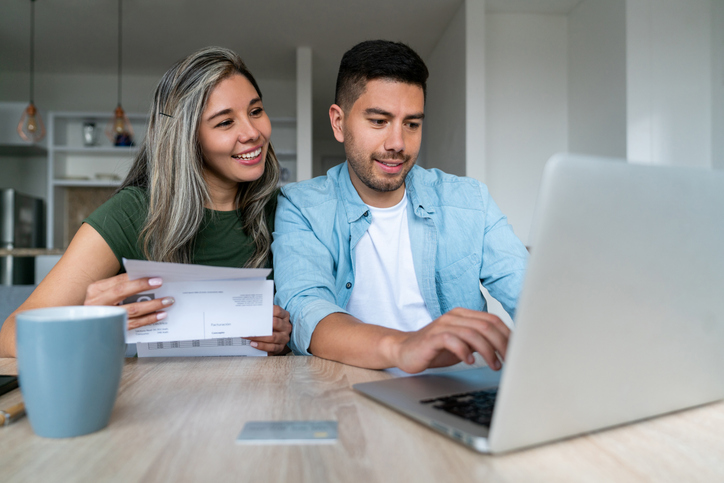 Happy couple paying bills online at home using a laptop