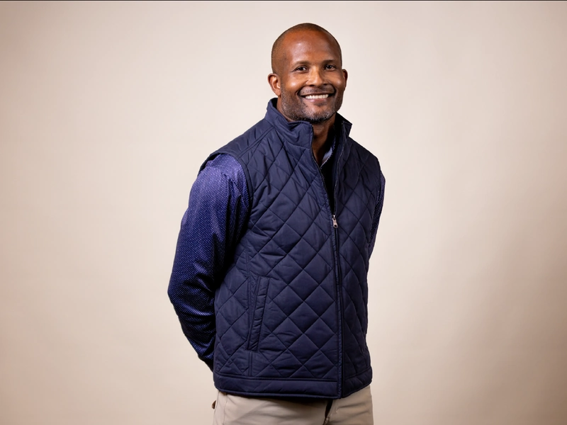 Champ Bailey of the Denver Broncos smiling in a navy quilted vest against a beige backdrop