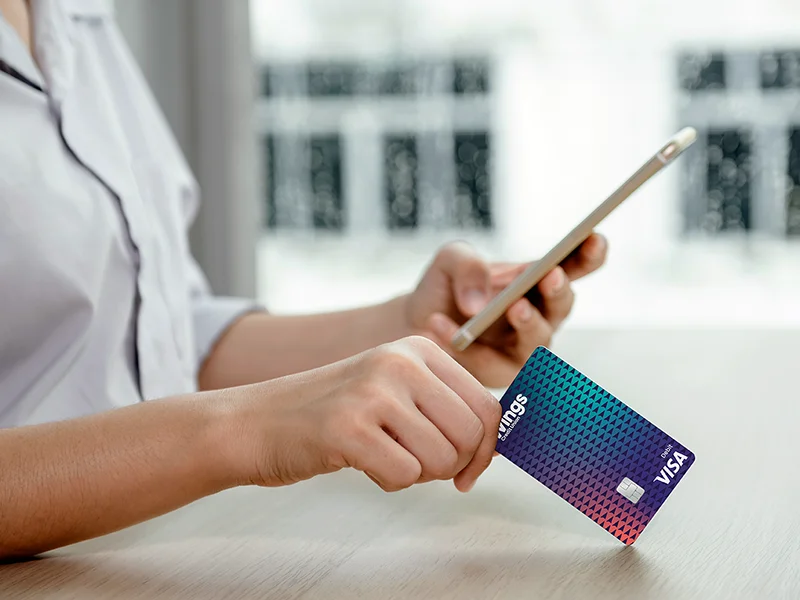 Close-up of a woman's hand holding an Wings debit card and a cell phone