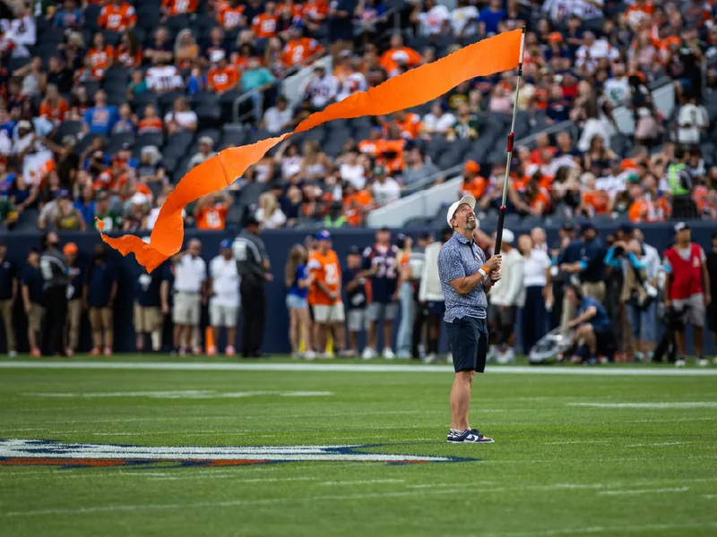 A man in a white cap waving a long orange flag on a football field