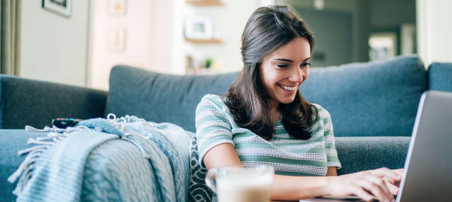 Woman sitting in front of her couch in the living room, working on her laptop.