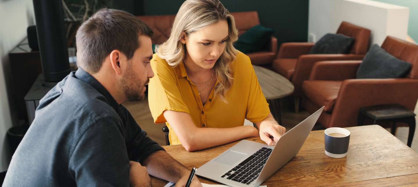 Man and woman sitting at a table reviewing their finances on a laptop.