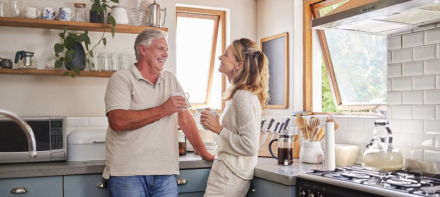 Older couple standing in their kitchen talking and drinking coffee