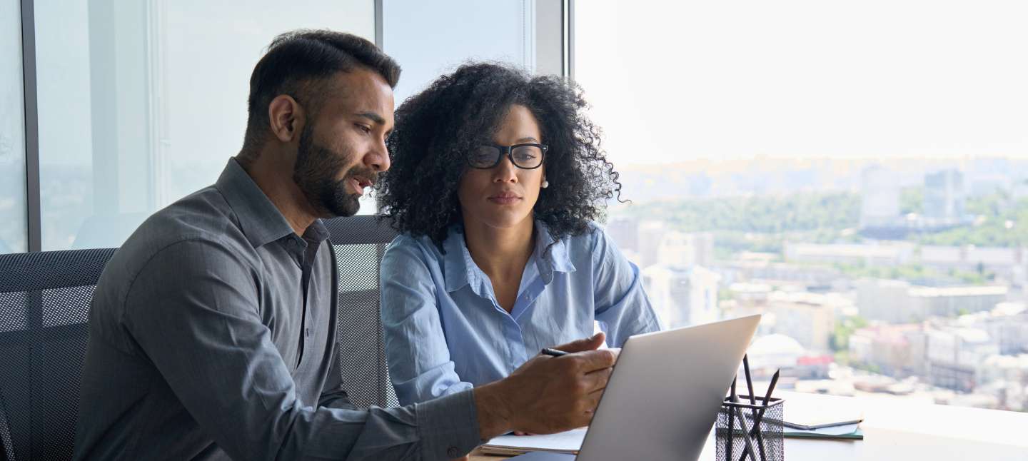 Multiethnic colleagues sitting at desk looking at laptop in office.