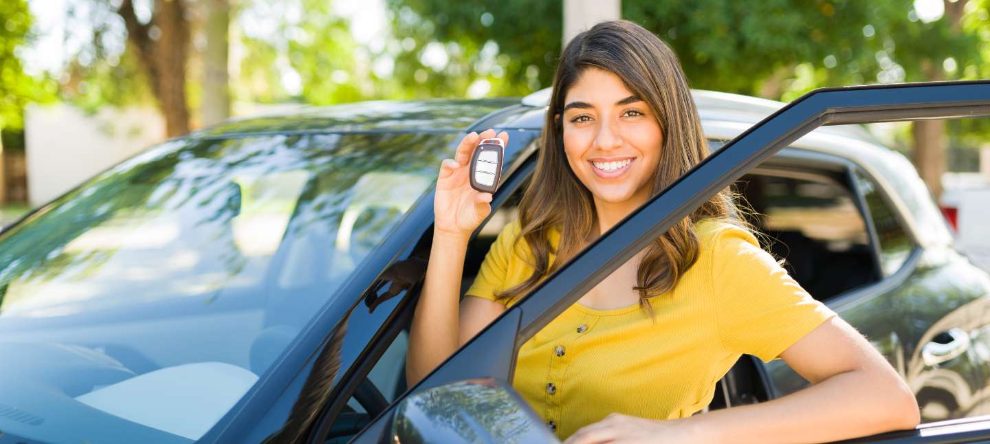 Young women smiling holding car key in front of red car.