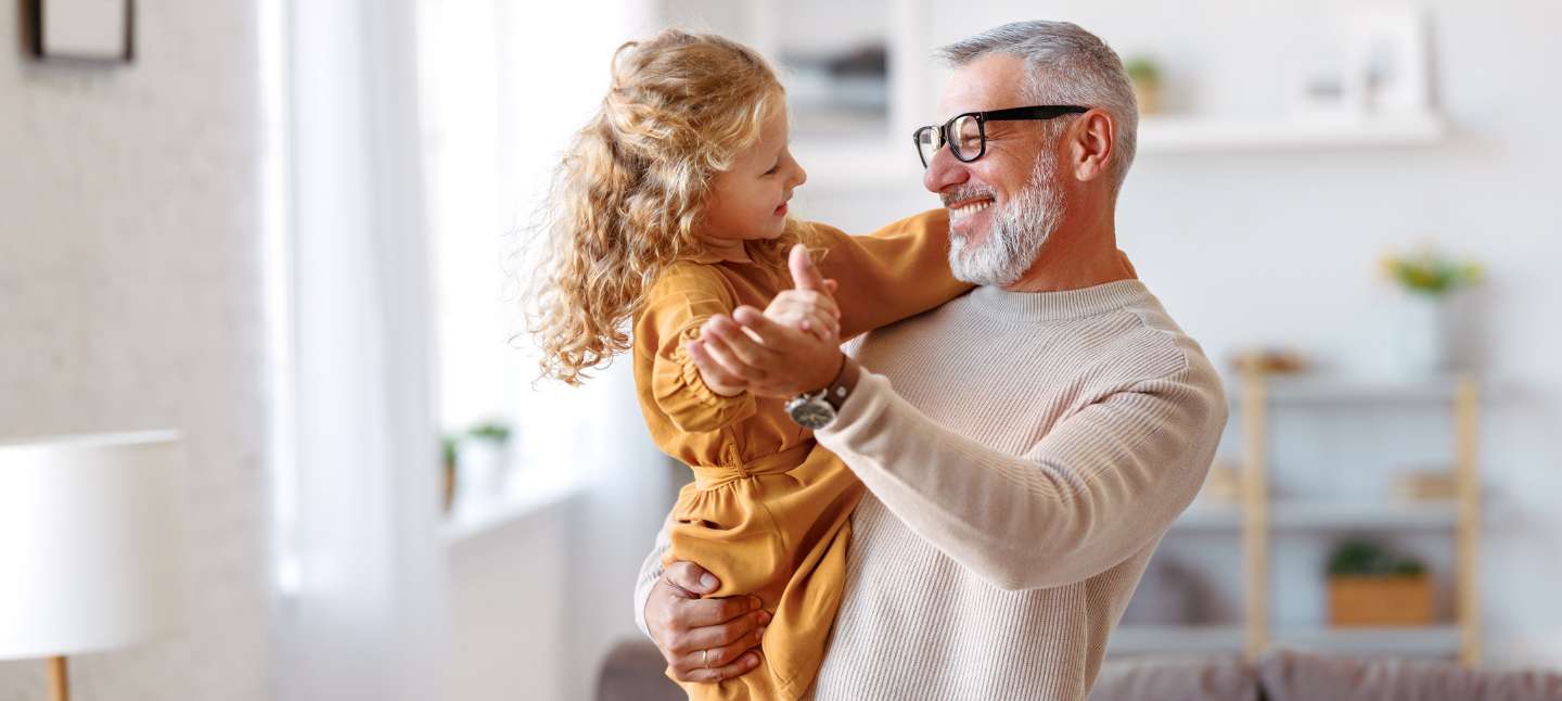 Granddaughter and grandpa holding hands while dancing together in living room at home.