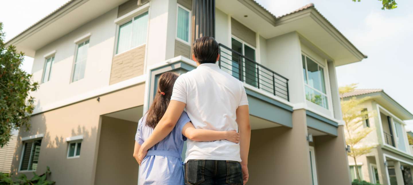 A man and woman holding each other while looking at their home