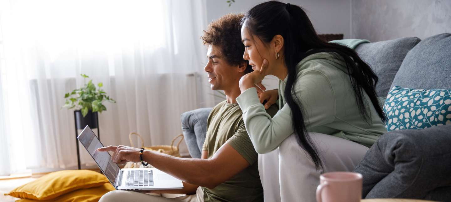 Wide shot of millennial couple lounging in their living room, planning out their finances and looking at their account via online banking.