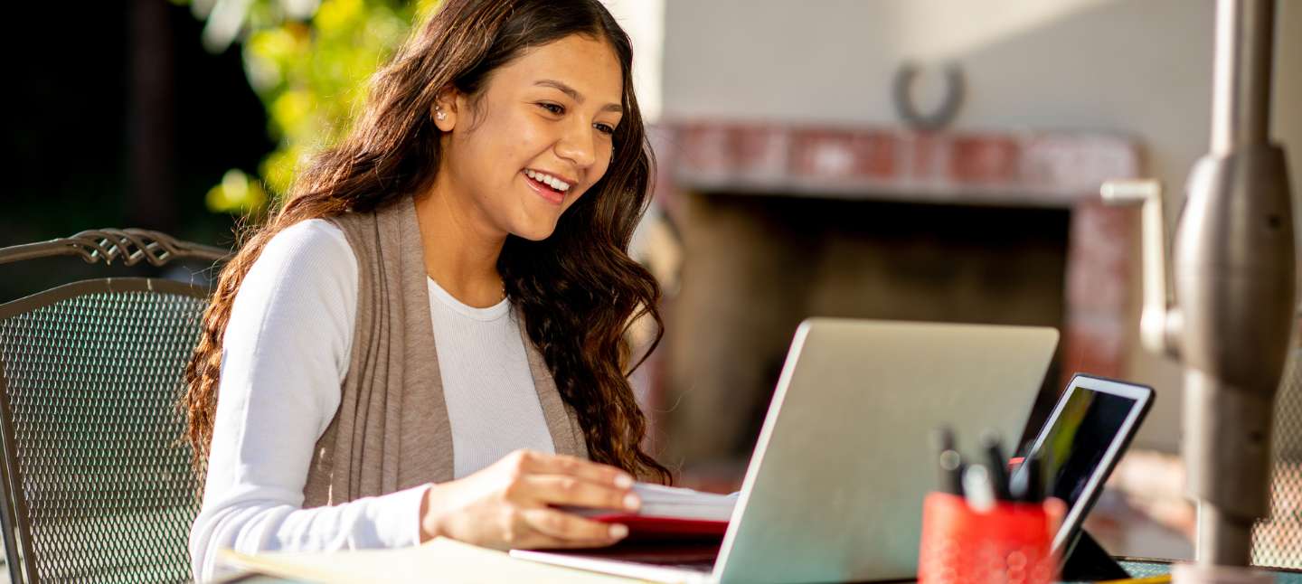 Young woman using her laptop at a table outside.