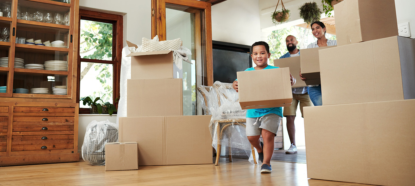 little boy running into house with a box and parents carrying boxed behind him