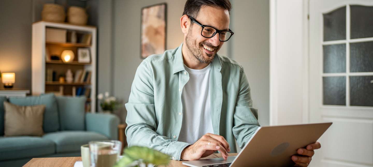 Man smiling at his laptop while working on his finances at home.