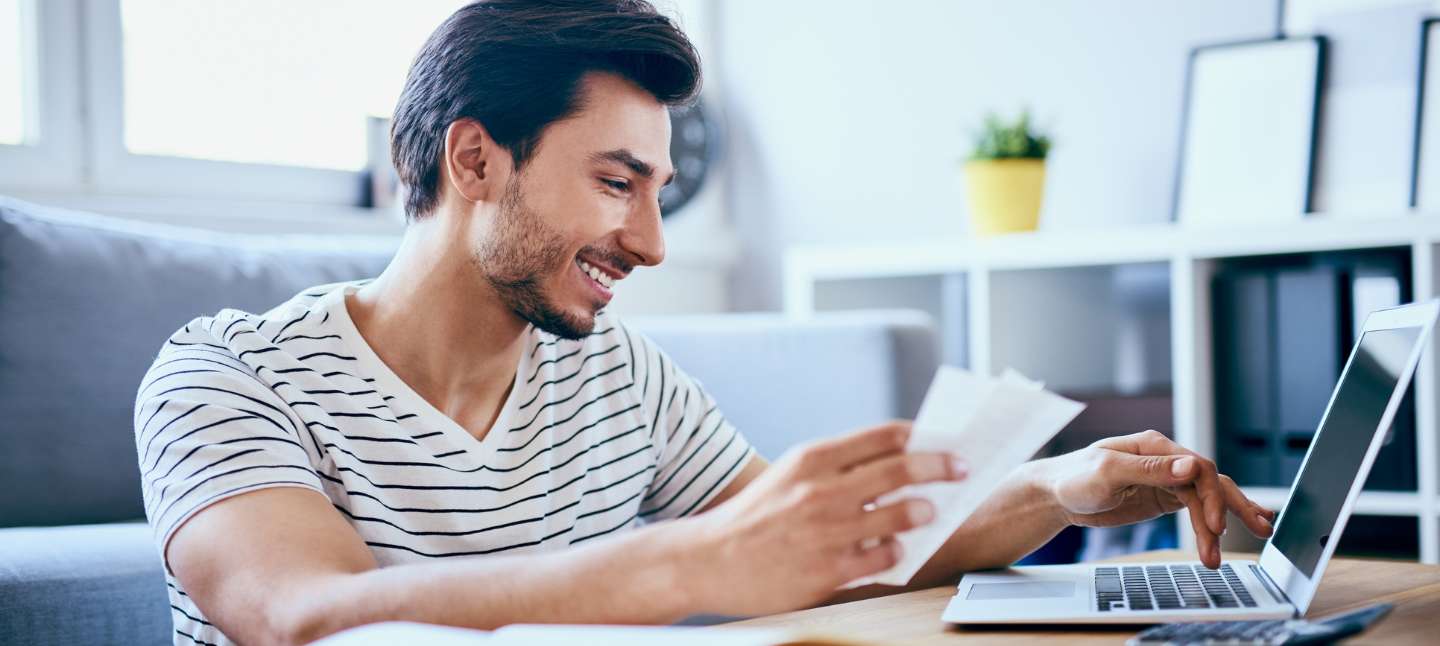 Happy man managing his finances on his laptop in living room