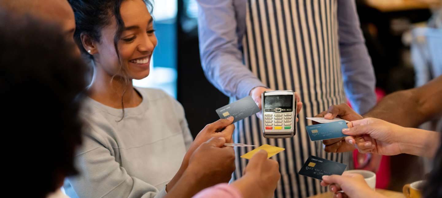 Happy group of friends paying with a credit card at a restaurant and splitting the bill.
