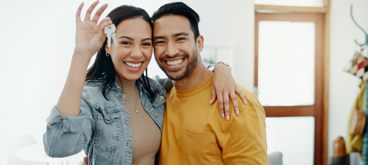A couple hugging and smiling while holding up keys to their home