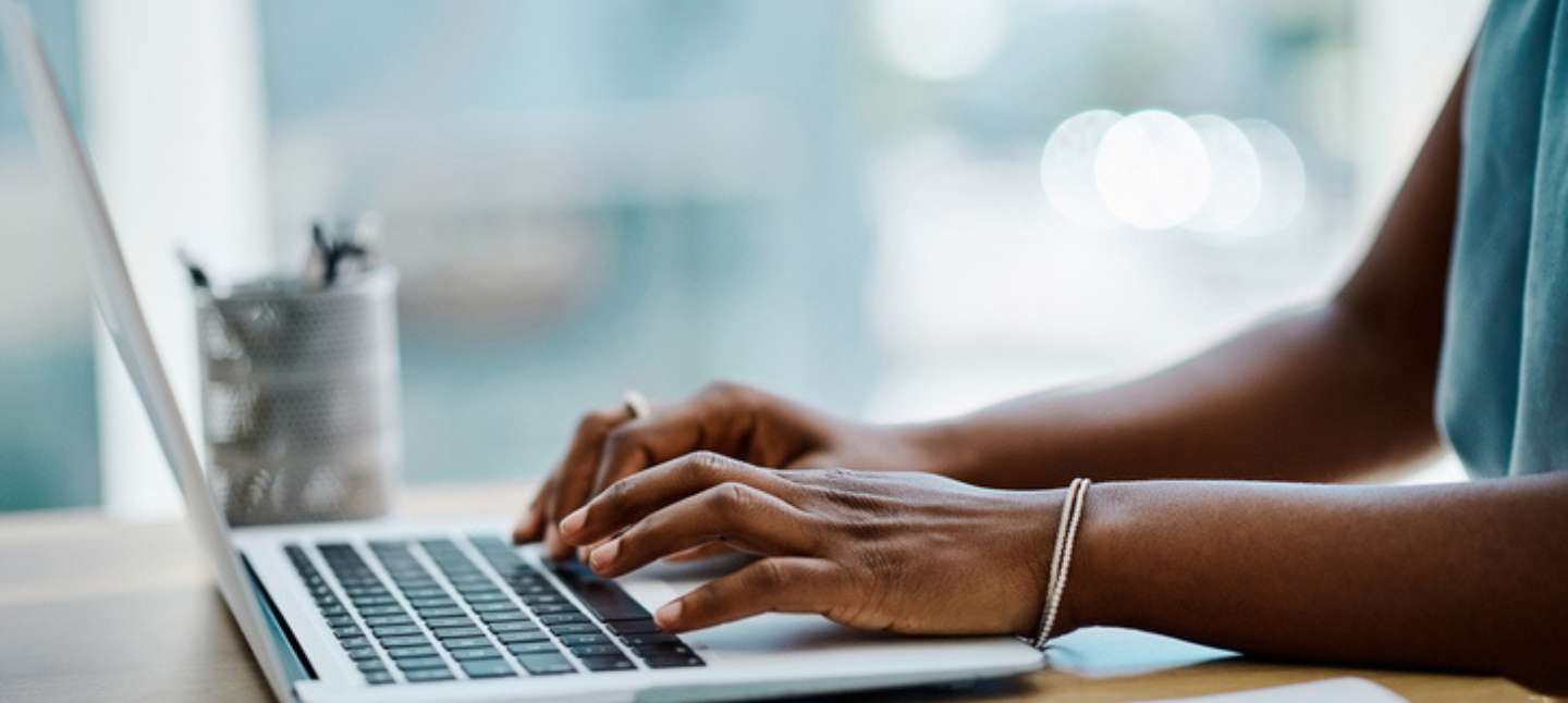 Closeup of a black businesswoman typing on a laptop keyboard in an office alone