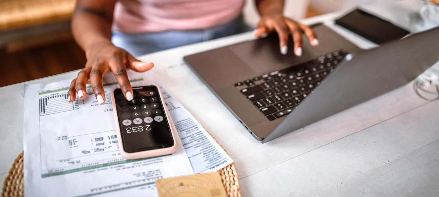 Woman managing home finances using smart phone calculator app and laptop