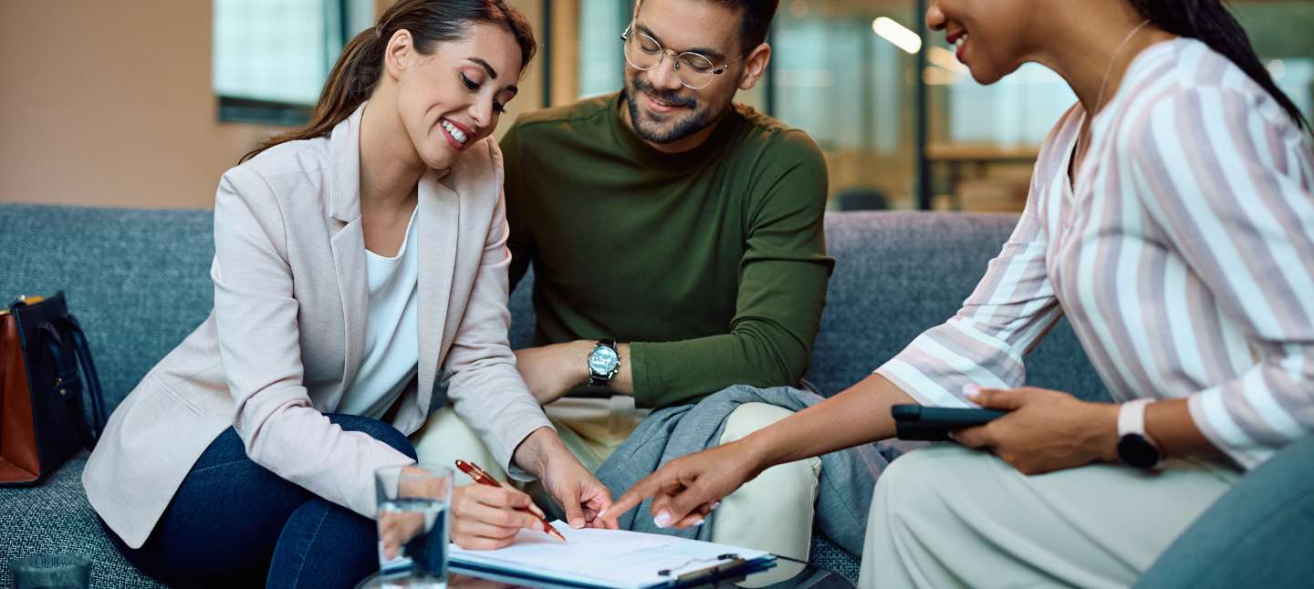 Happy woman and man signing a contract while in a meeting with their mortgage loan officer.