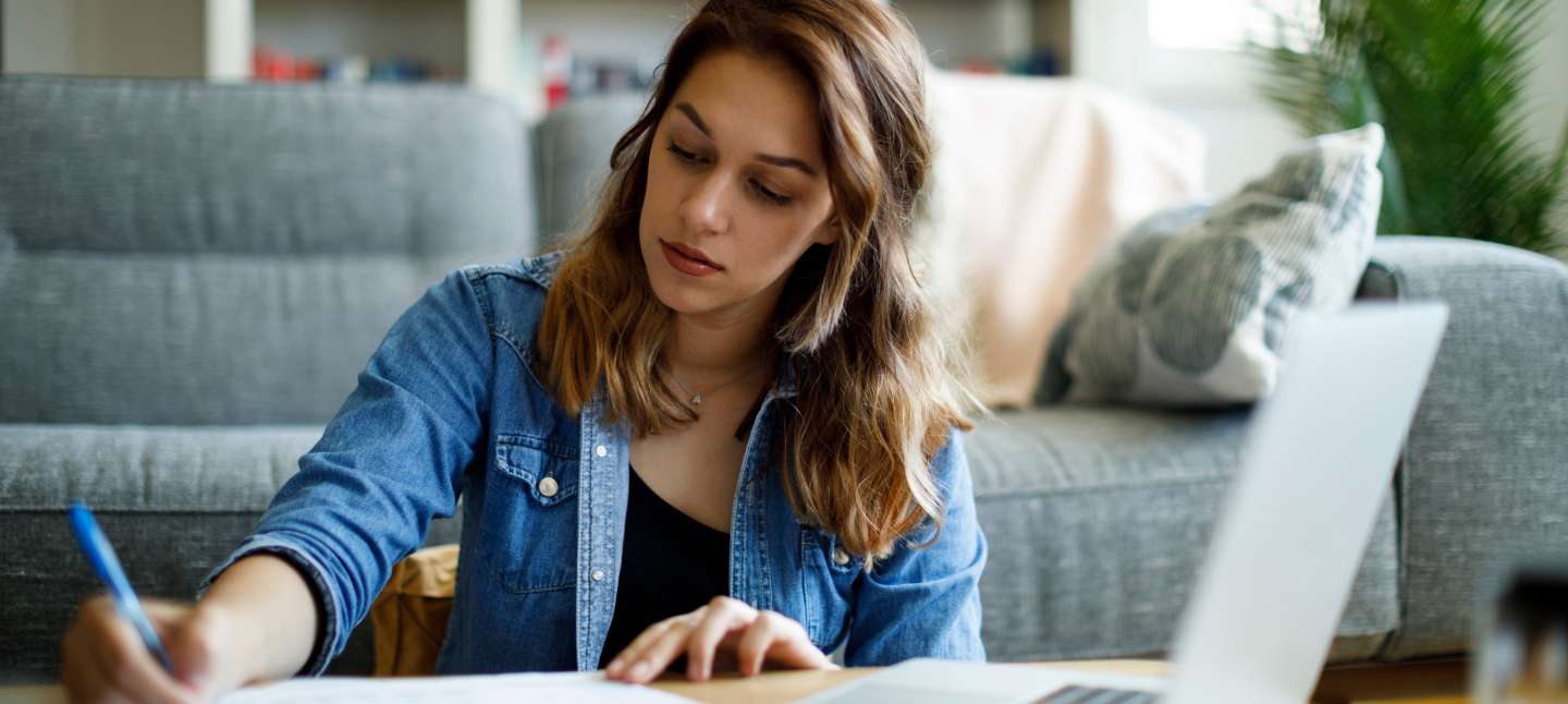Young woman writing down notes while organizing her finances in the living room.