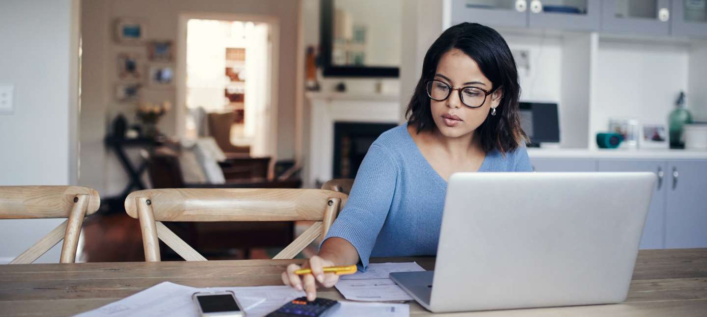 Young woman using a laptop and calculator while managing her finances at home.