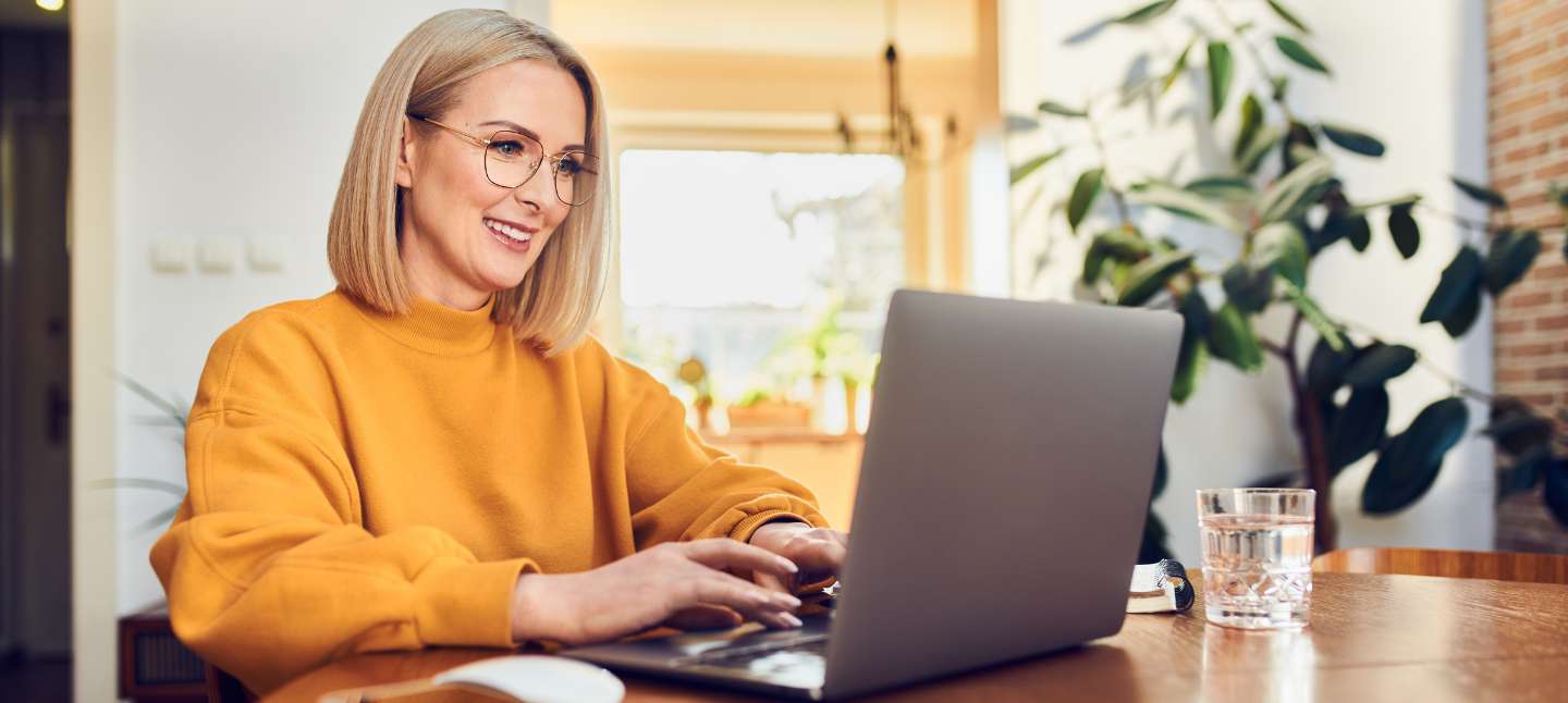 Portrait of middle aged woman sitting at dinning with laptop working at home.