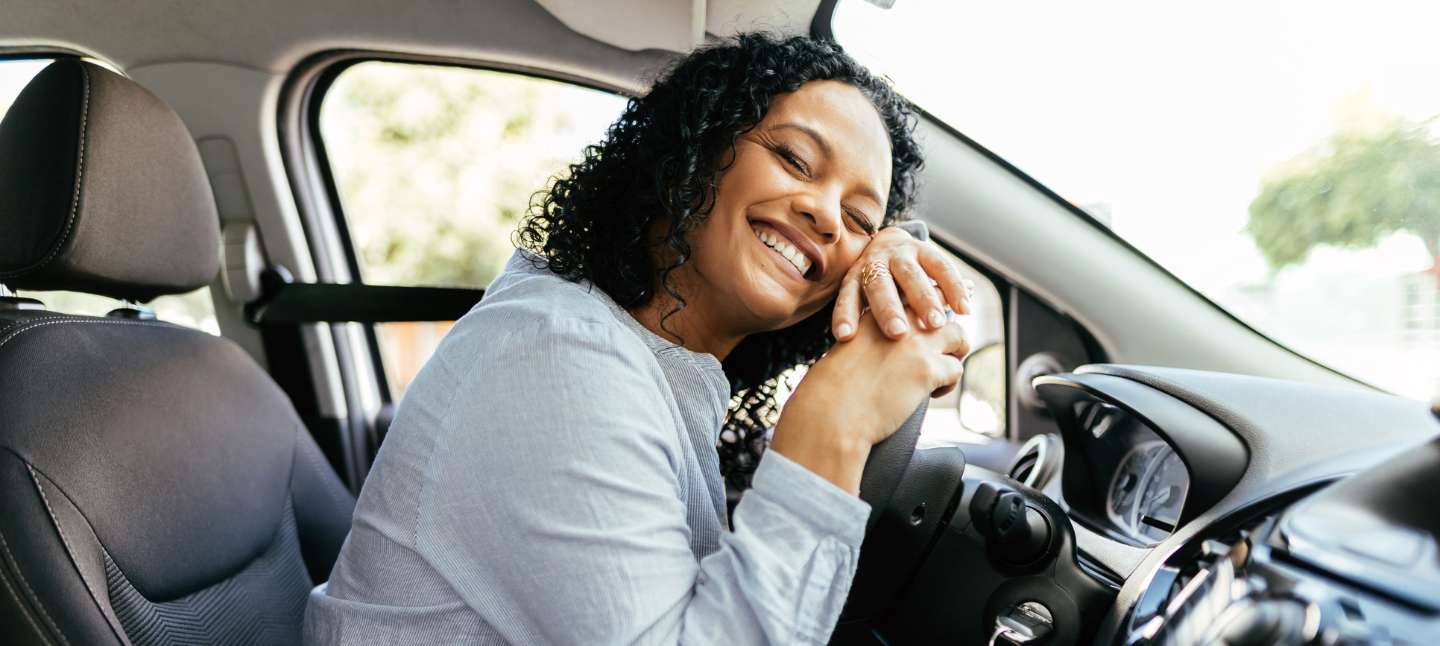 Young and cheerful woman enjoying new car hugging steering wheel sitting inside.