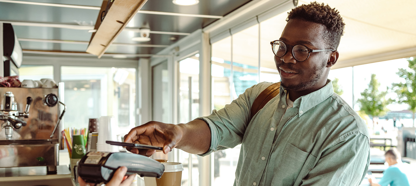 Young man using his phone to pay for a coffee