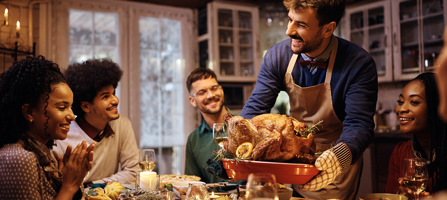 Young happy man serving Thanksgiving turkey to his friends at the dining table