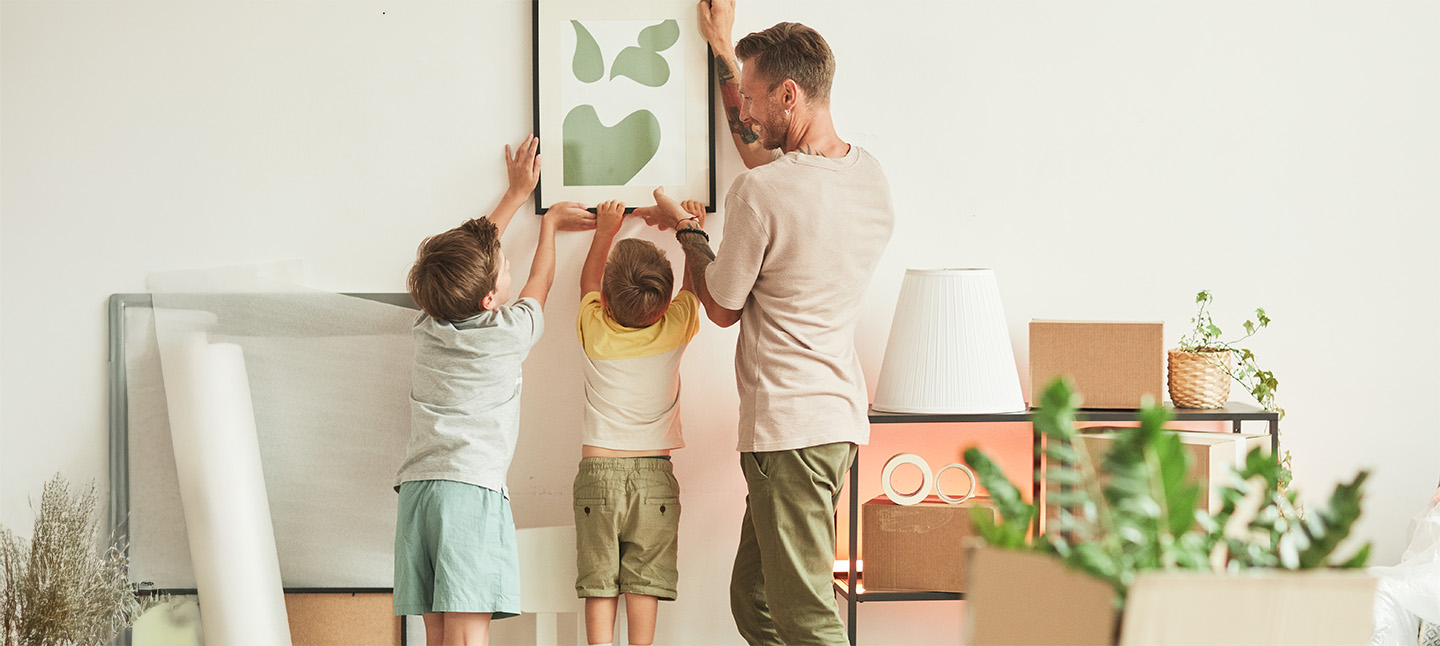 A father and sons hanging a picture in the livingroom
