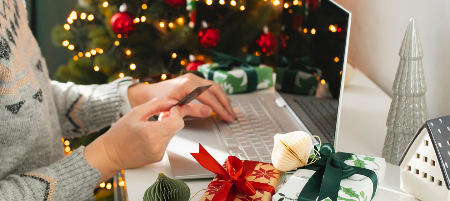 Female hand holding card while using her laptop to online shop for holiday gifts.