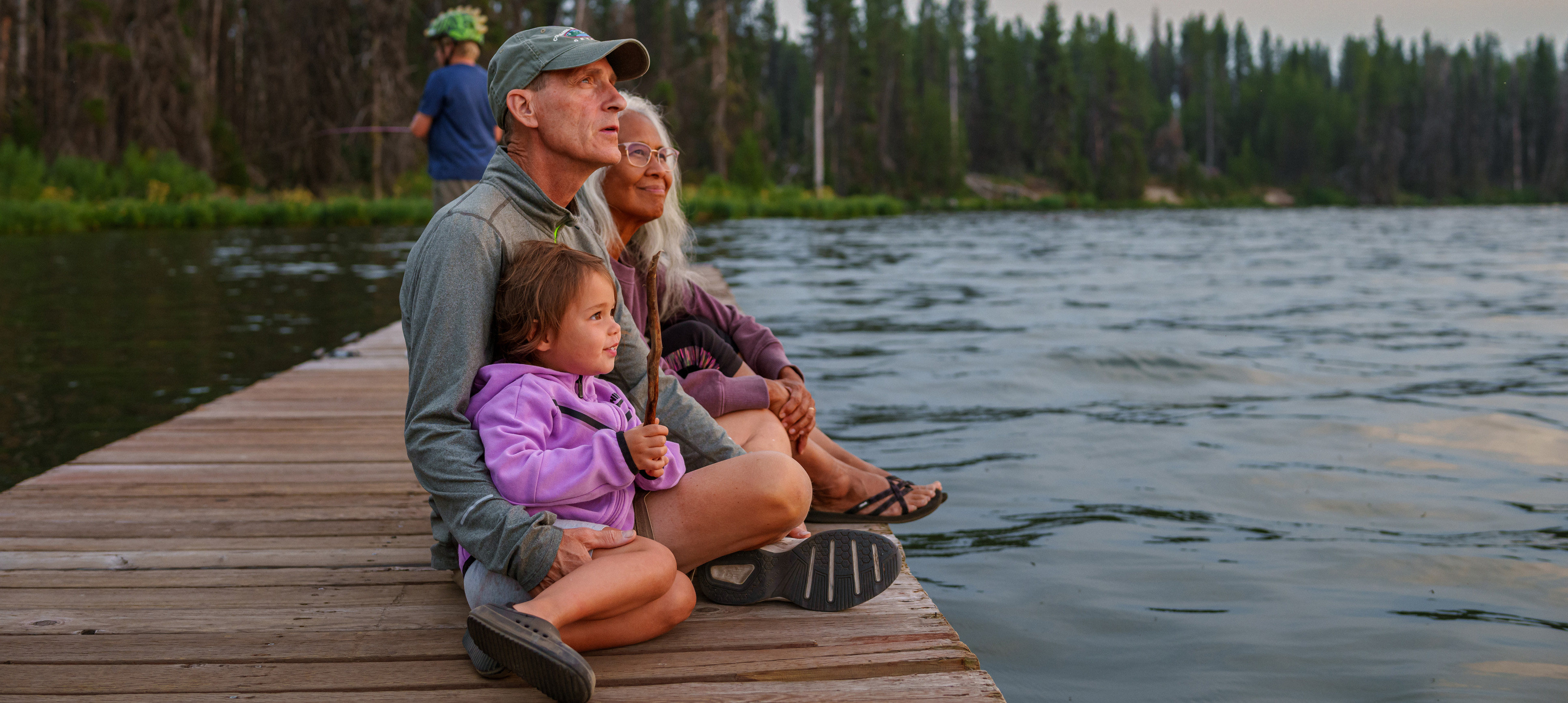 Grandparents and granddaughter enjoy sunset on a lake dock
