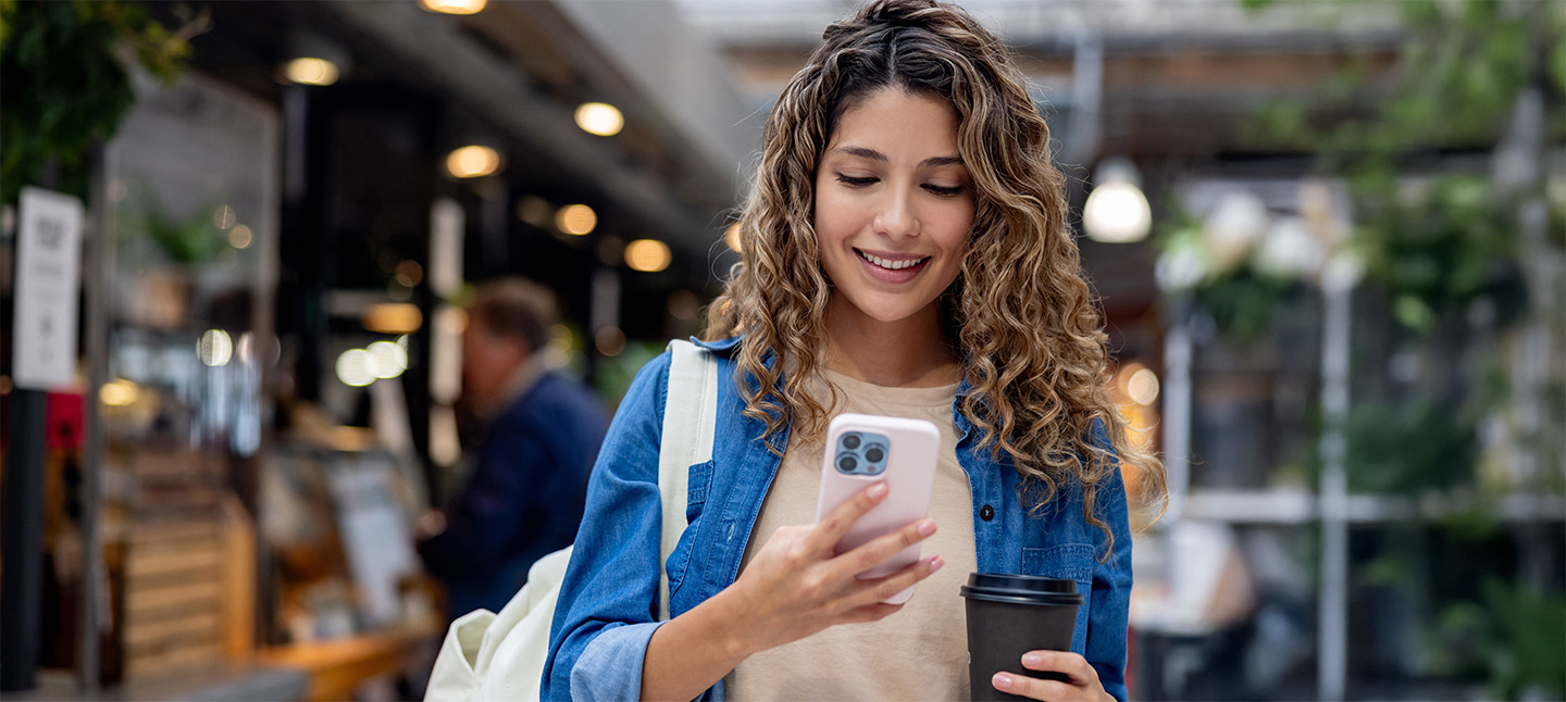 Woman at a shopping center holding a cup of coffee while texting on her cell phone
