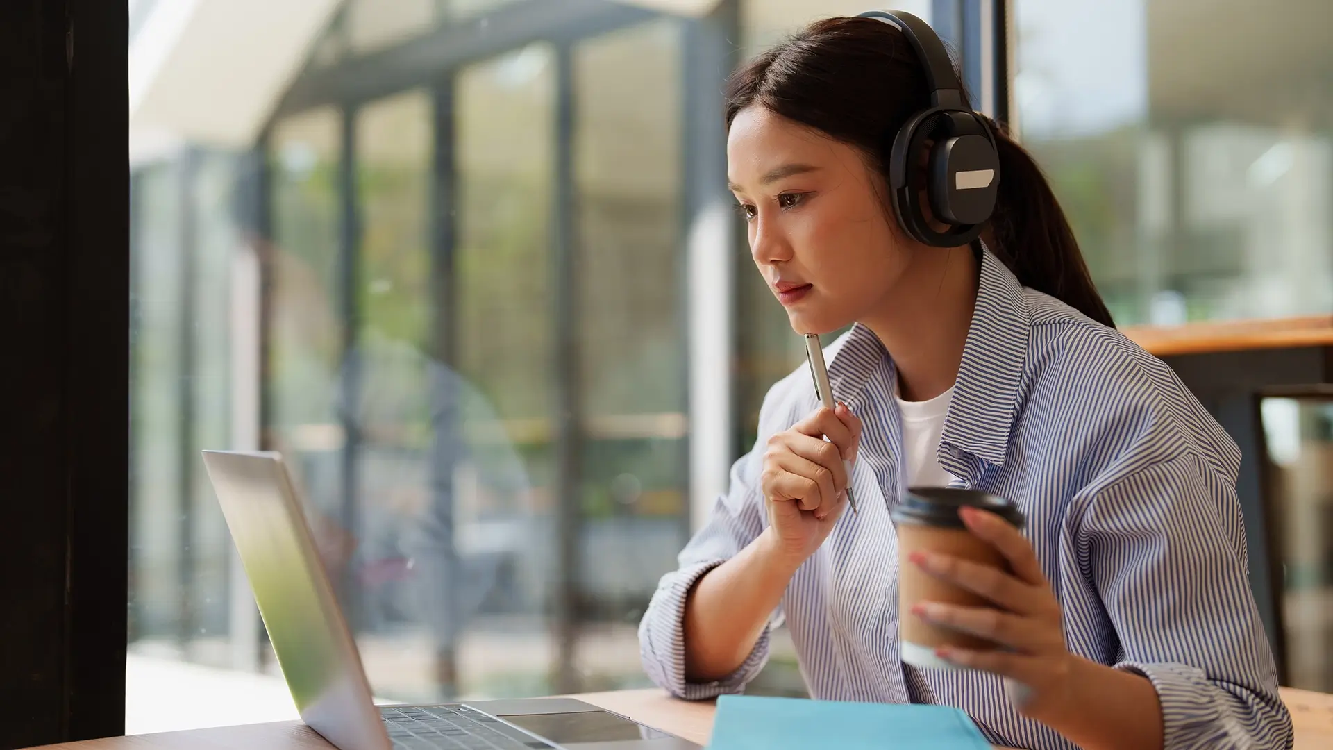 A college student learning online, wearing headphones and drinking coffee