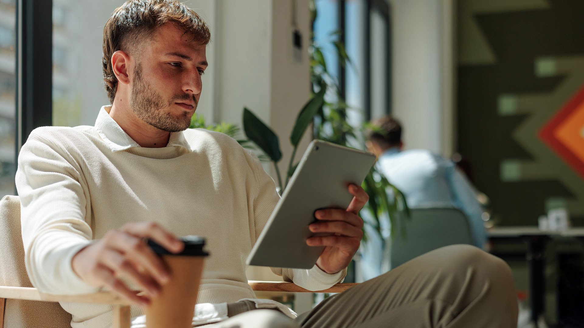 Young man reading on his tablet while drinking coffee