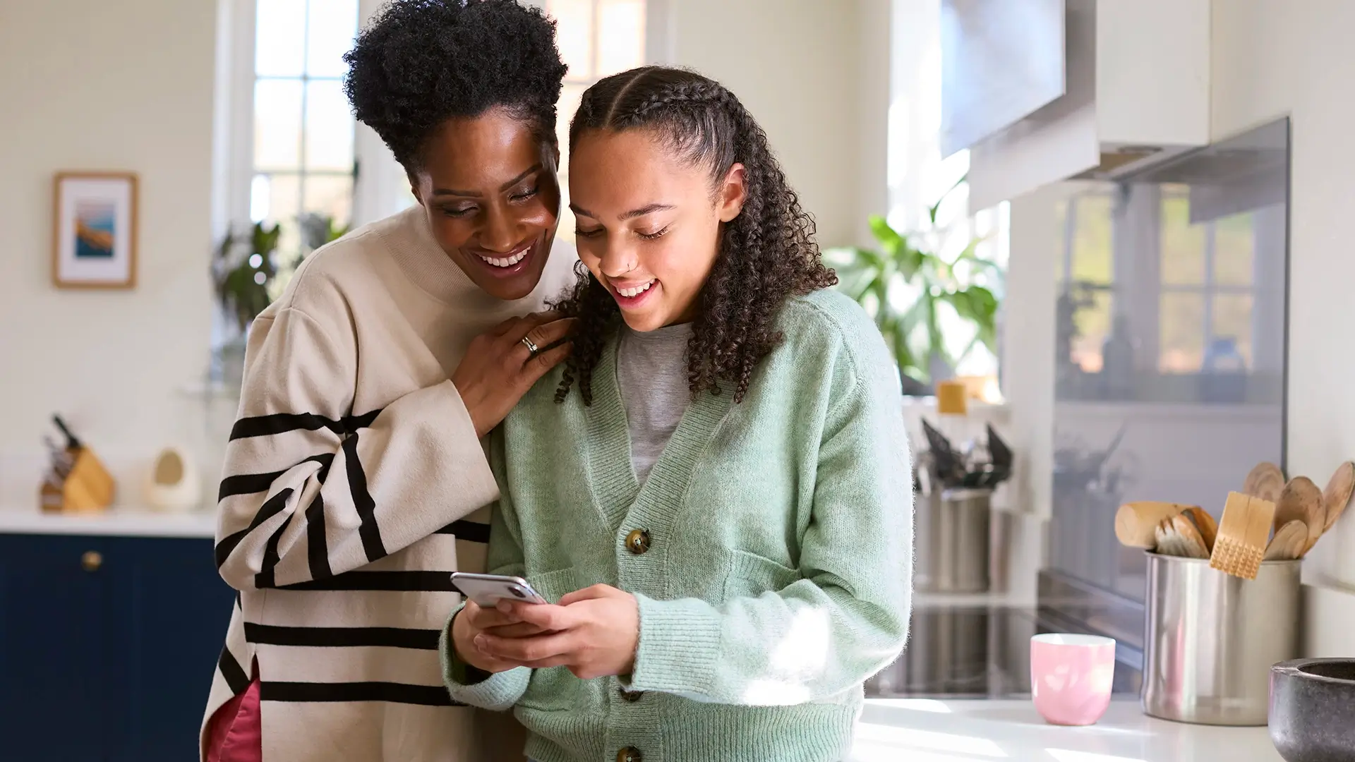 Mother Talking With Teenage Daughter At Home Looking At A Mobile Phone Together 