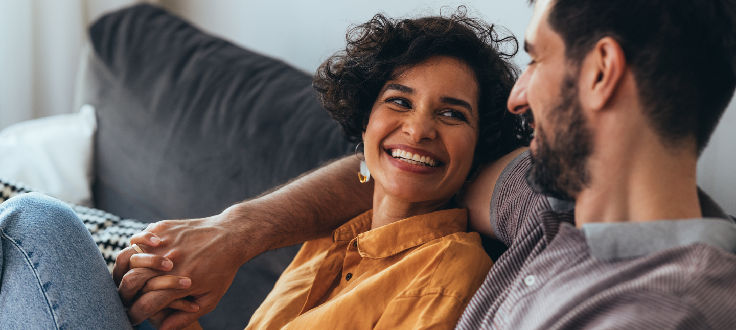A smiling Latin-American woman and her Caucasian boyfriend sitting on a couch enjoying spending their leisure time together.