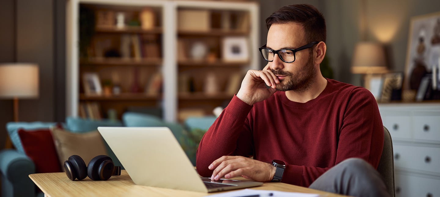 A young adult male resting his head on his hand while looking at his laptop