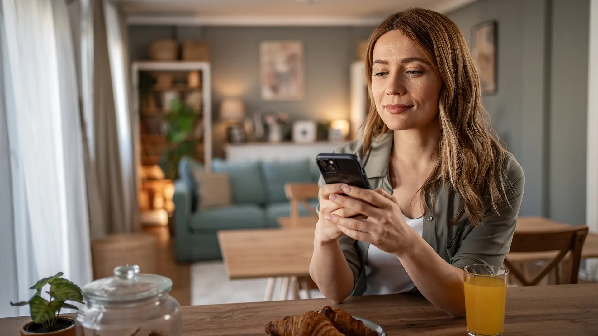 A young woman on her phone reading while having breakfast