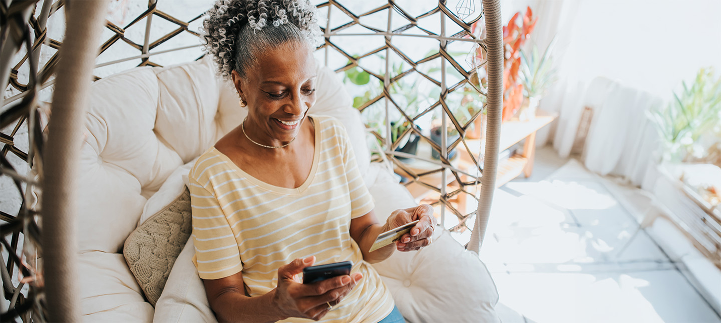An older woman using her credit card and holding her cell phone in the living room of the house