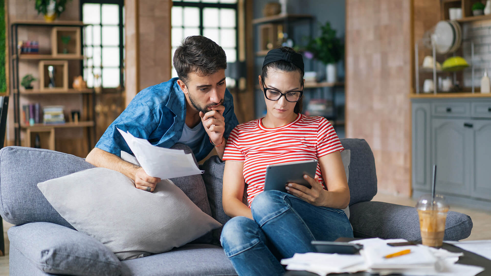 A couple calculating bills at home using a tablet and a calculator