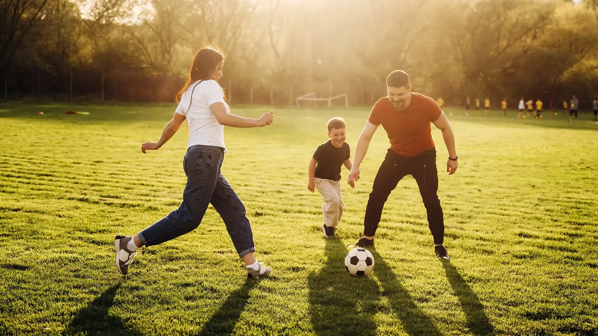 Family of mother, father and son playing soccer on the field