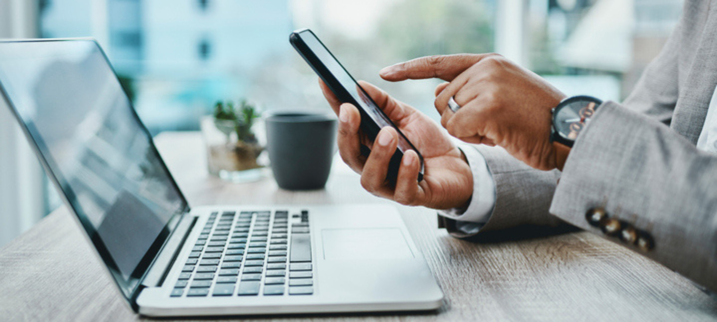 Shot of an unrecognizable businessman using a smartphone and laptop in a modern office