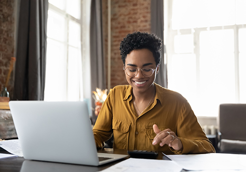 Woman sitting at a table using a laptop and calculator 