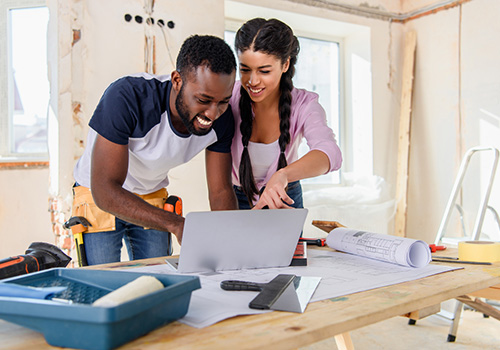 A man and woman looking at a computer while renovating a room